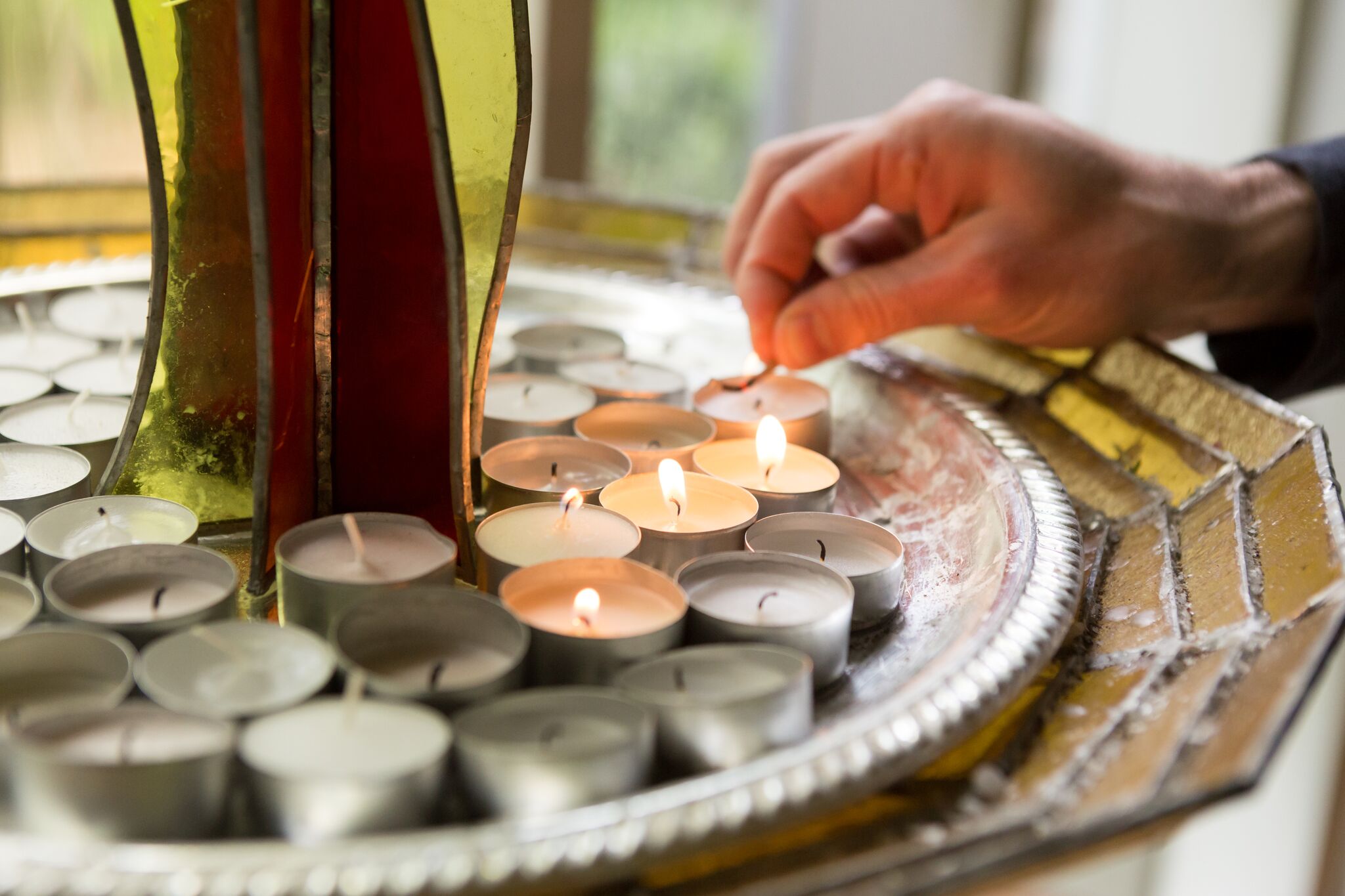 Hand holding match, lighting a platter full of tea light candles.