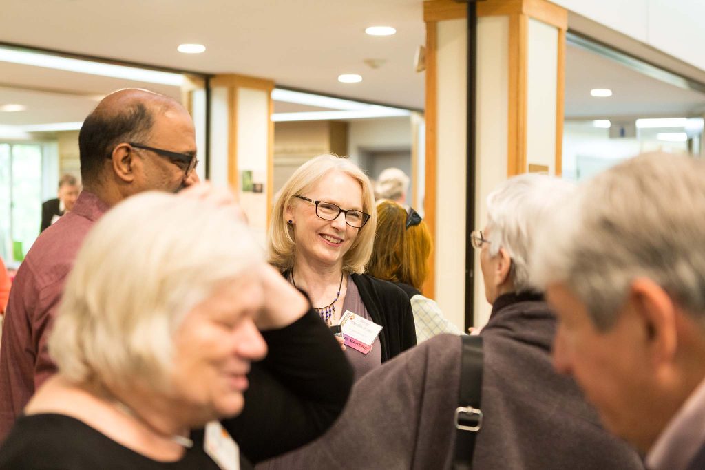 Blonde woman wearing glasses stands in center of group of people.