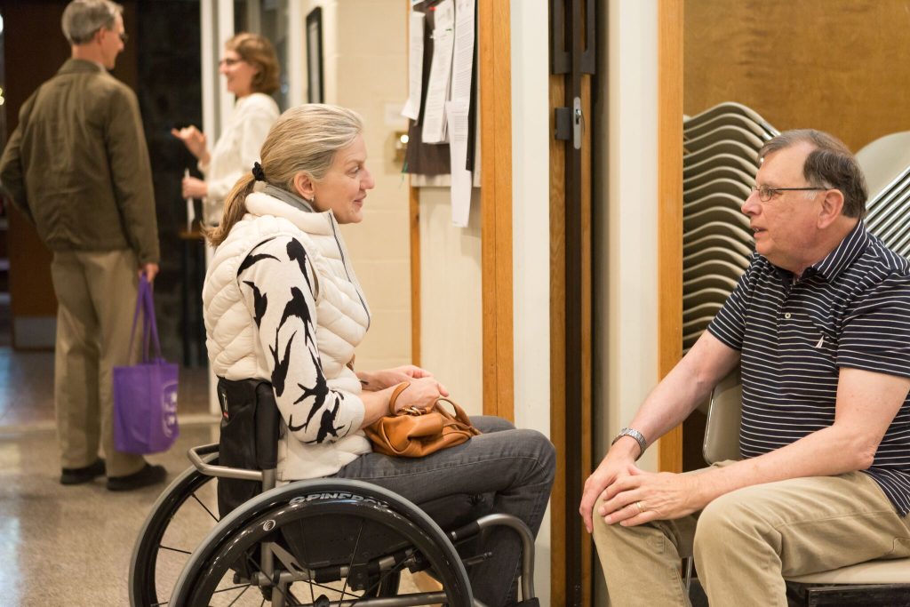 Women in wheelchair in conversation with seated man.