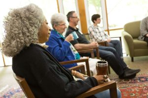 Four adults sitting on chairs. One is sipping from a mug.