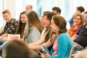 Three young adult women sit in audience, smiling.