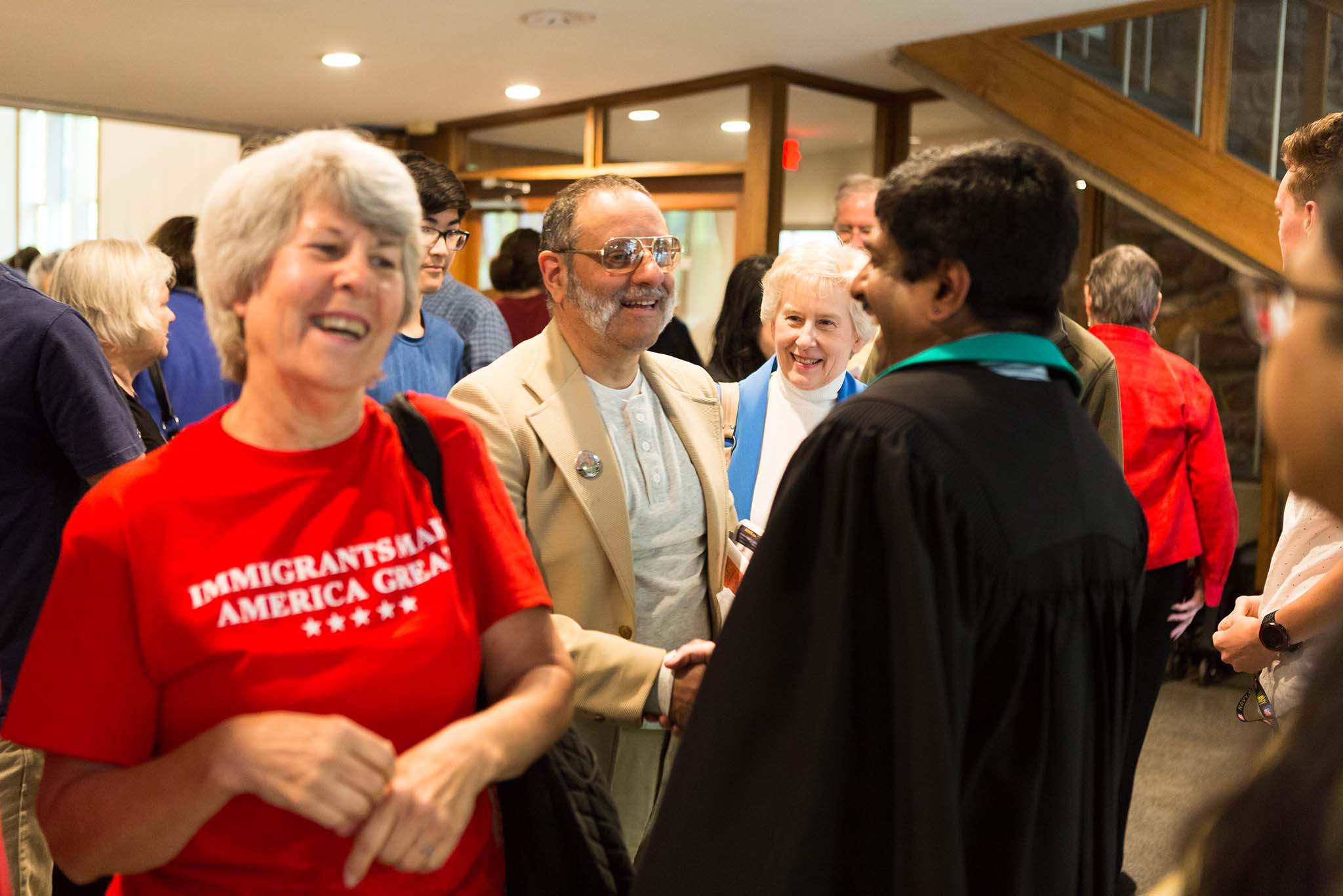 Group of smiling people. Woman on left wears a red t-shirt with the words "Immigrants Make America Great"